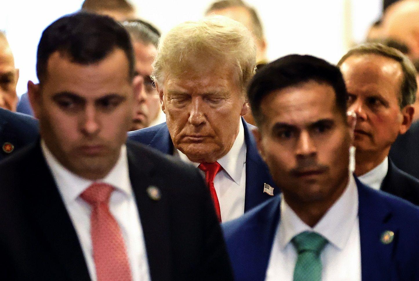 Trump caminhando com feiçãõ séria e rodeado de assessores e seguranças