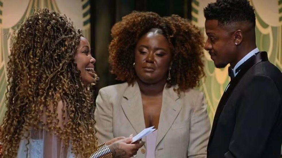 Fotografia colorida mostra casal negro em frente a uma ministra durante cerimônia