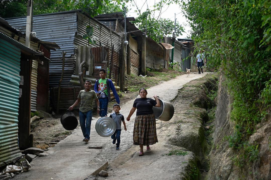 Personas caminan con cacerolas vacías en un asentamiento de Guatemala. 