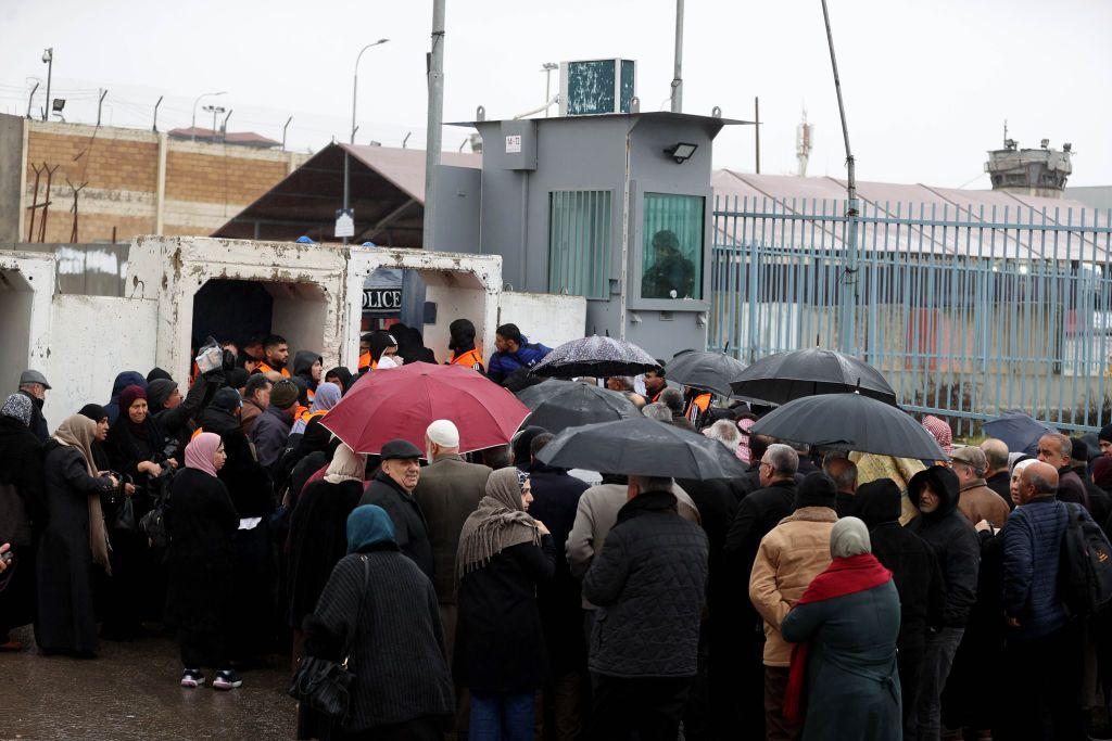 جمع مكتظ لنساء ورجال فلسطينيين قرب حاجز قلنديا العسكري، وعدد منهم يحمل مظليات. الأجواء ماطرة.