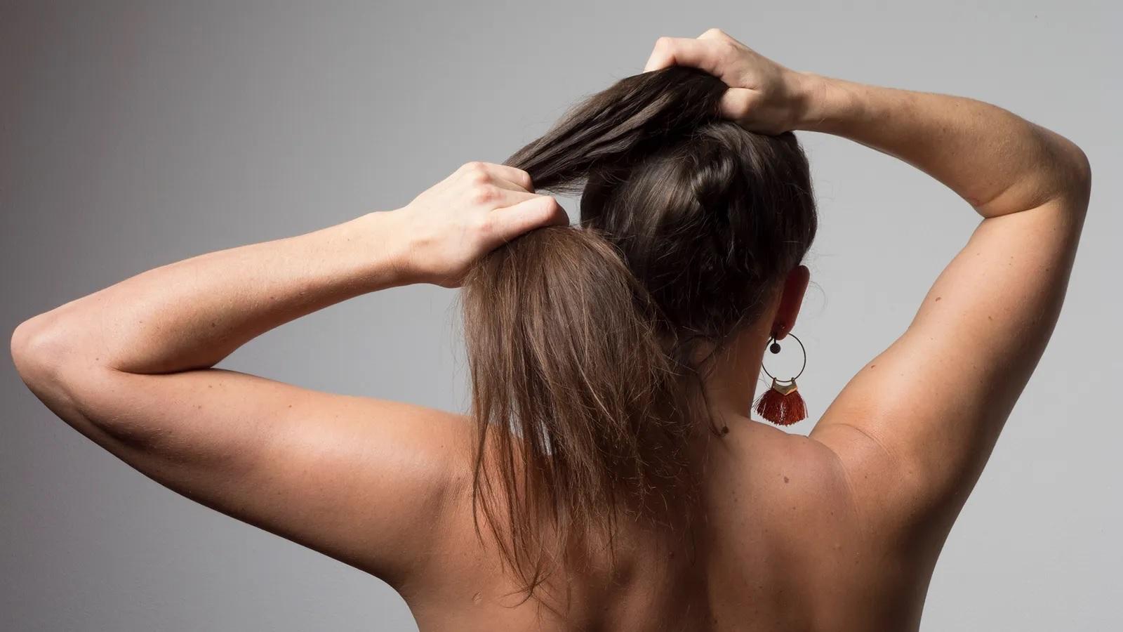 Foto mostra pessoa de pele clara de costas segurando cabelo comprido