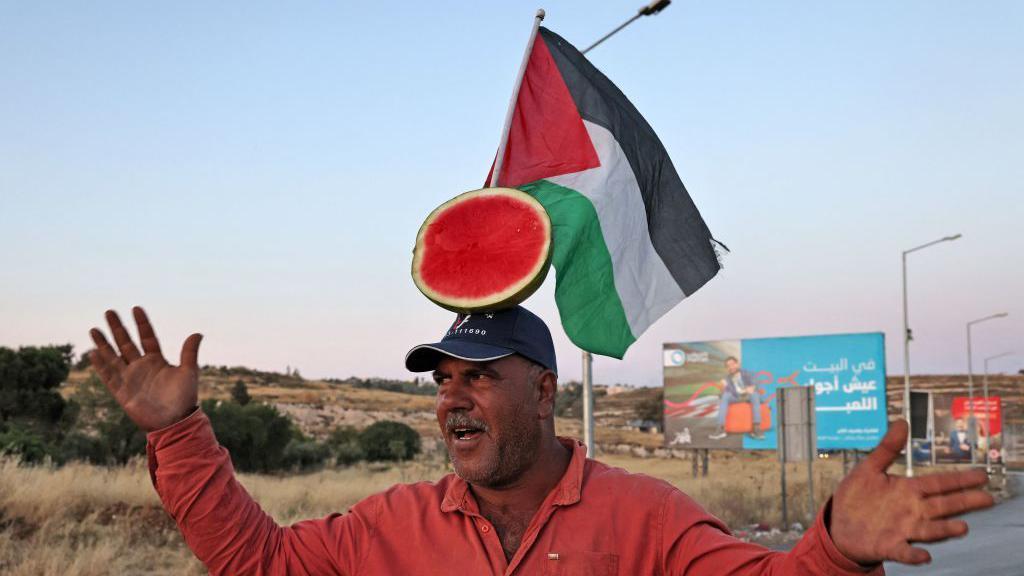 Seorang penjual semangka Palestina mengadakan pertunjukan untuk menarik pelanggan, di sebuah jalan di pintu masuk utara kota Ramallah, pada 5 Juni 2023.