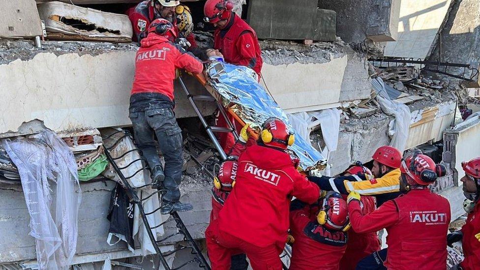 Equipes de resgate carregam uma mulher resgatada de um prédio que desabou após um terremoto em Kahramanmaras, na Turquia