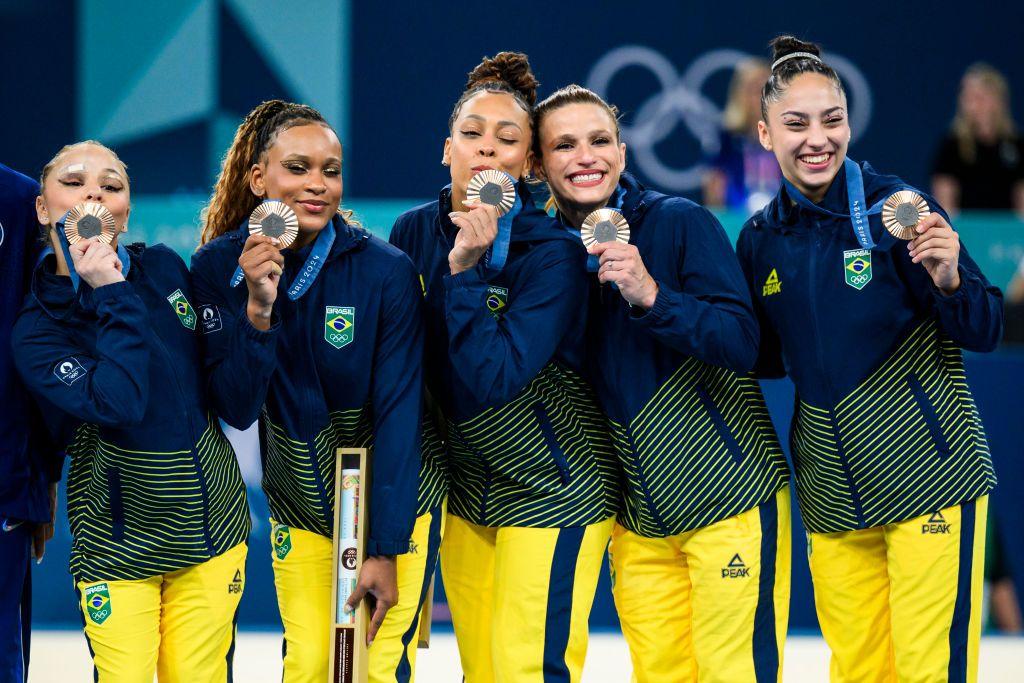 Cinco atletas brasileiras sorrindo e mostrando medalha