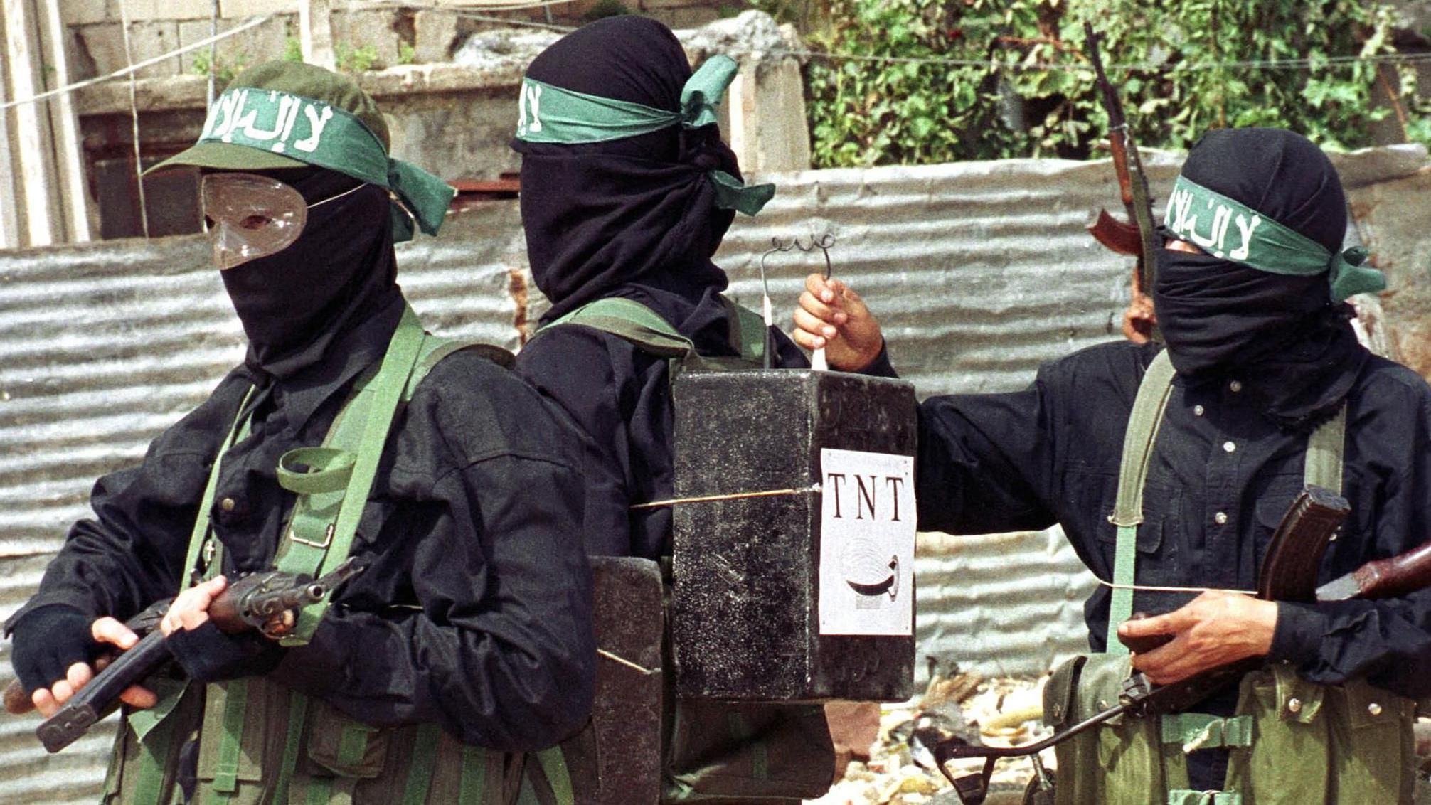 مسلح فلسطيني يربط صناديق تحمل علامة متفجرات تي إن تي على ظهر أحد رفاقه.