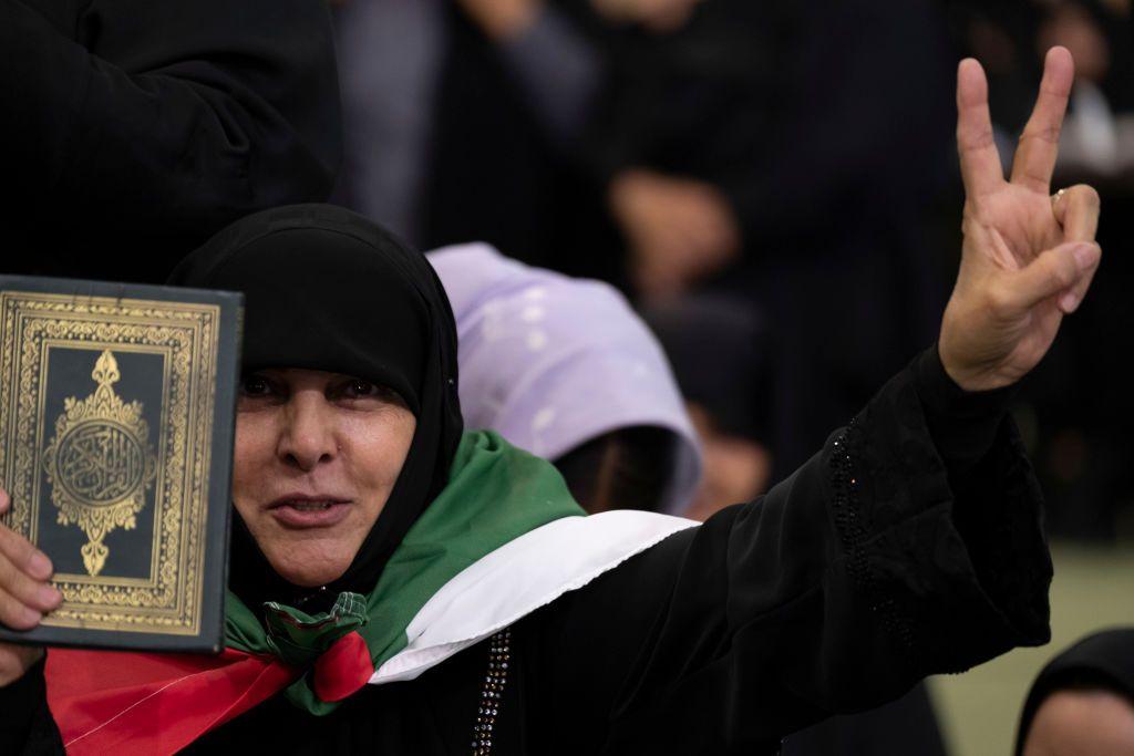 Una mujer vestida con velo negro porta un Corán y una bandera palestina.