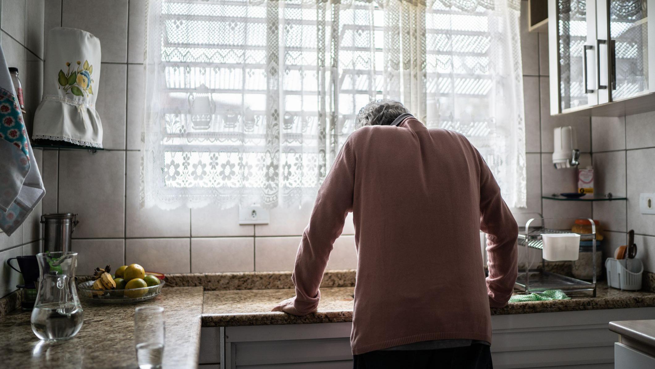 Um homem mais velho, que parece exausto, se apoia numa pia de cozinha