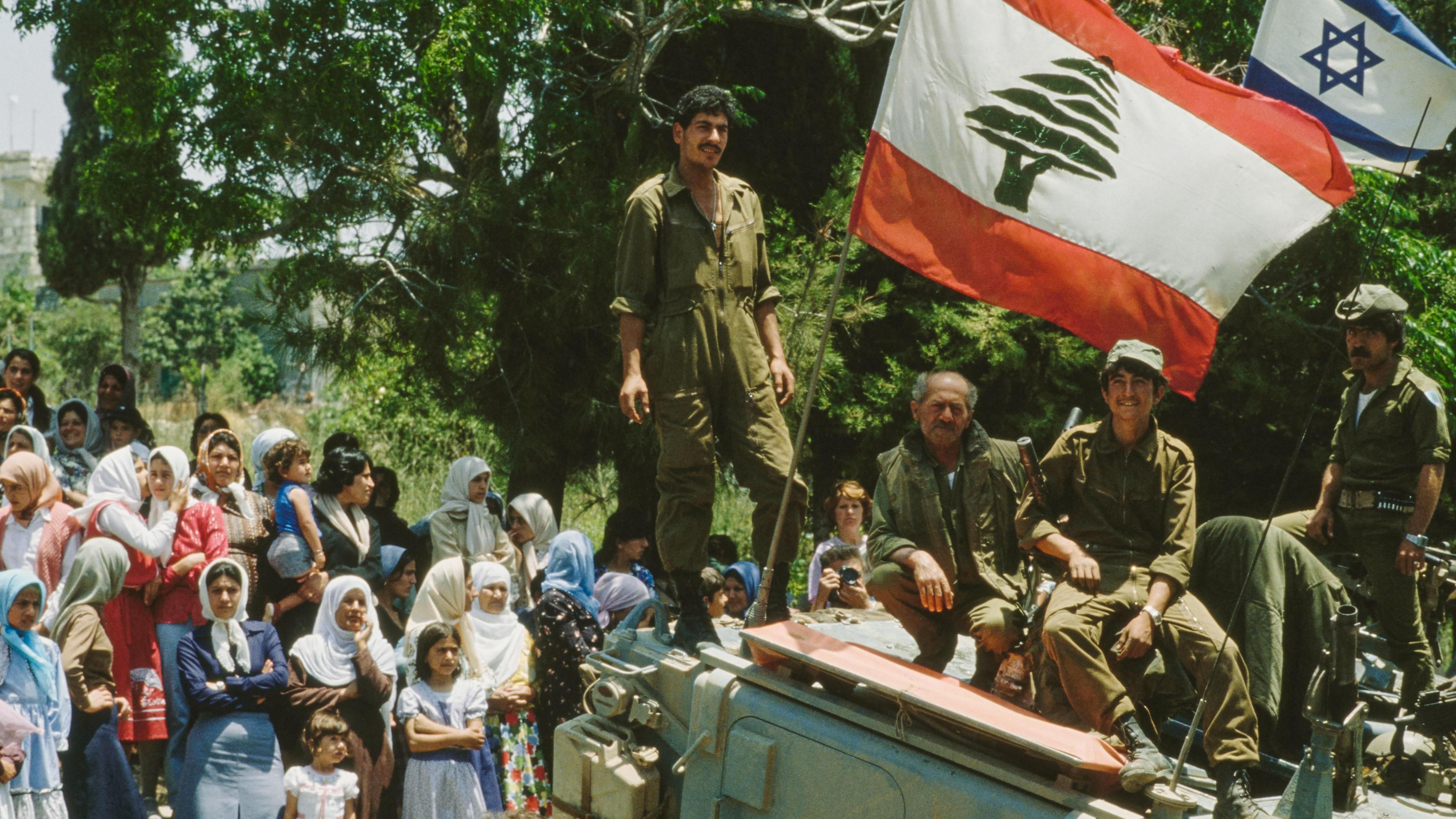 جنود إسرائيليون على سطح مركبة مدرعة، ونساء يقفن على الطريق خلفهم في يونيو/حزيران 1982