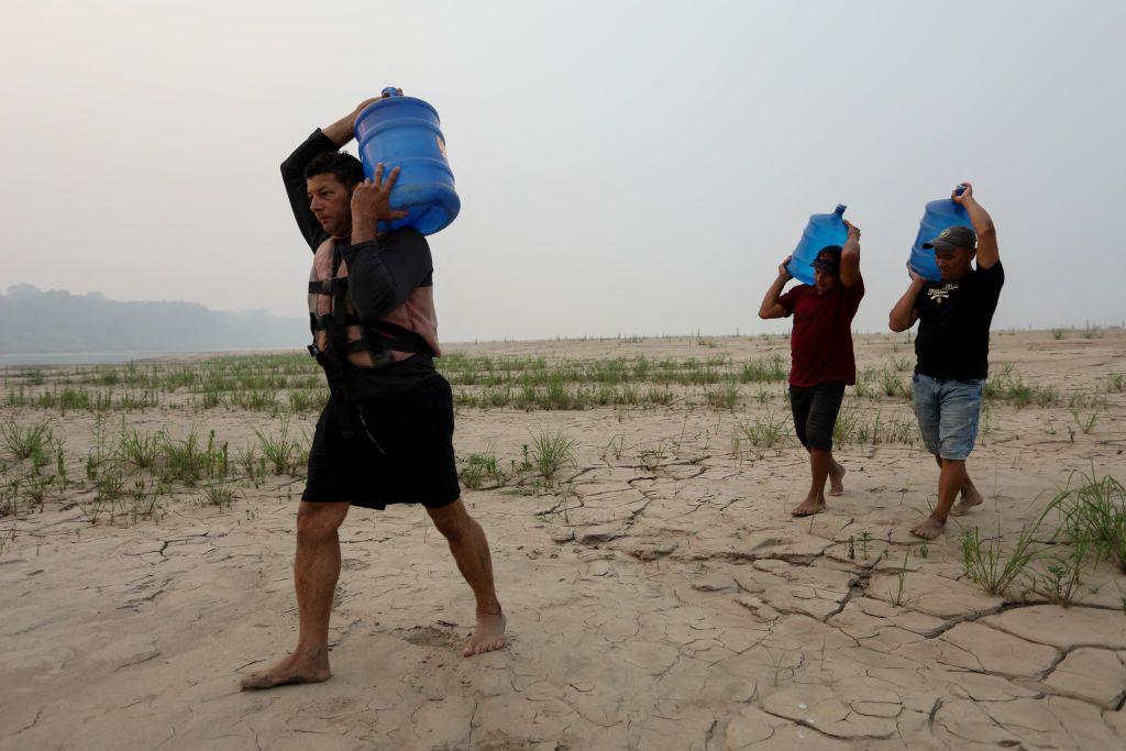 Una foto de personas que transportan galones de agua potable en un terreno seco a lo largo del río Madeira en estado de Amazonas, Brasil, el 7 de septiembre de 2024.