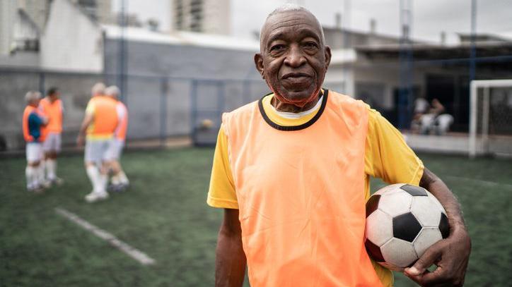 Homem em campo de futebol segurando bola com a mão