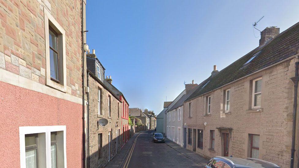 Uma rua ladeada por casas em Eyemouth, com carros estacionados 