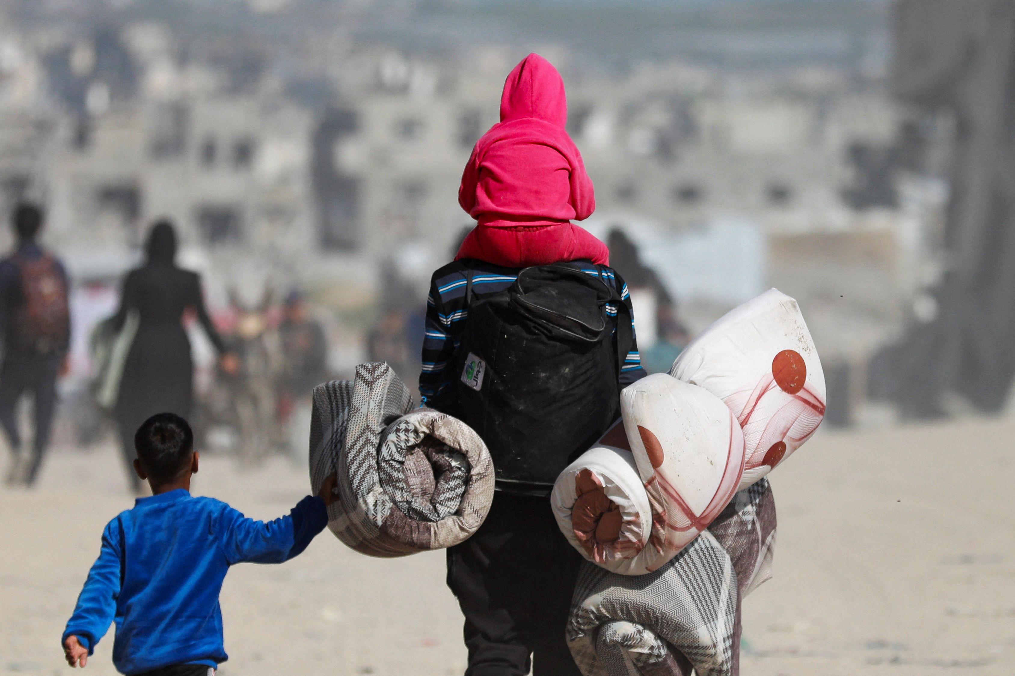 Un hombre con dos niños llevando unos colchones. 