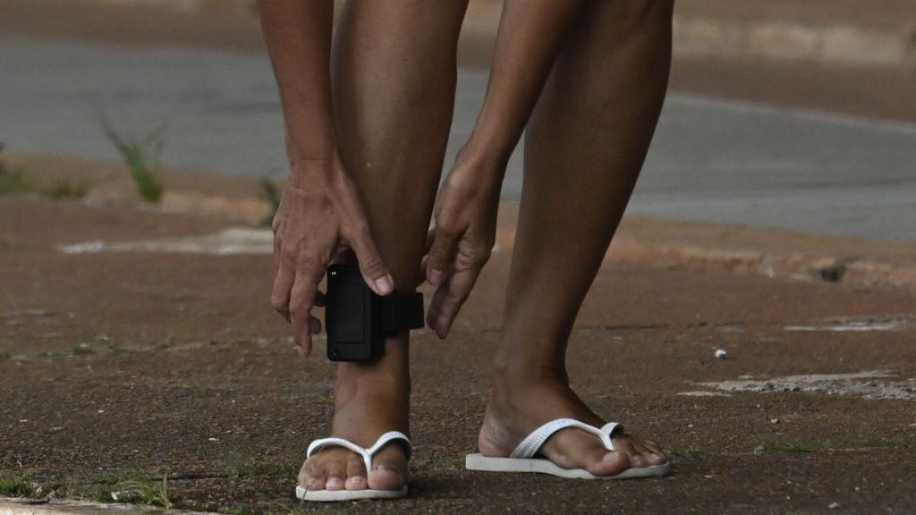 Pés de pessoa negra de chinelo usando tornozeleira eletrônica