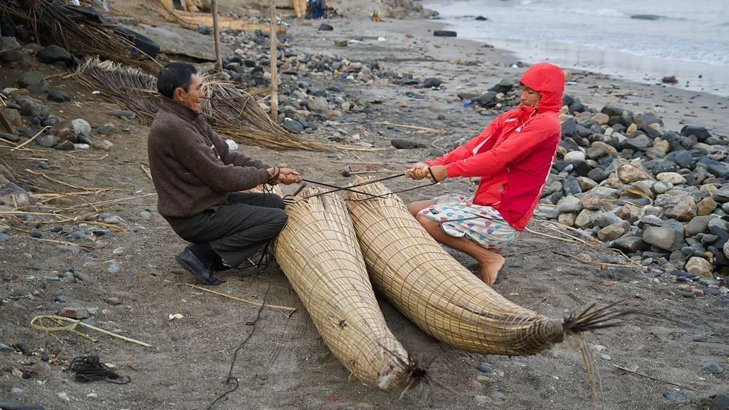 Dois homens manuseando o barco na praia