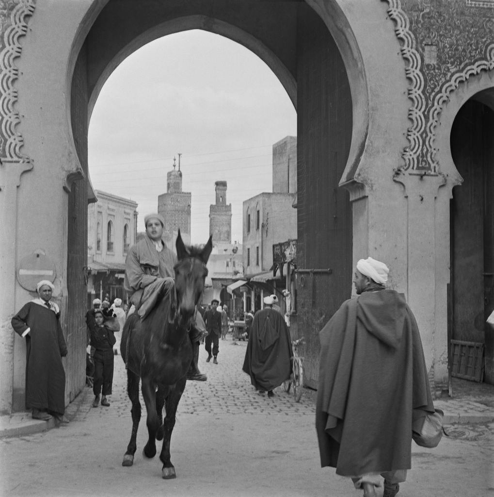 رجال يمرون عبر بوابة باب بوجلود في مدينة فاس، المغرب، فبراير 1954