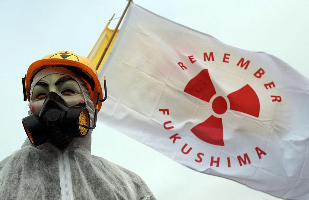 متظاهر ملثم يقف أمام الأعلام عند بوابات محطة هينكلي بوينت للطاقة النووية لإحياء الذكرى الأولى لكارثة فوكوشيما في اليابان في 10 مارس/ آب 2012 بالقرب من بريدجواتر، إنجلترا.