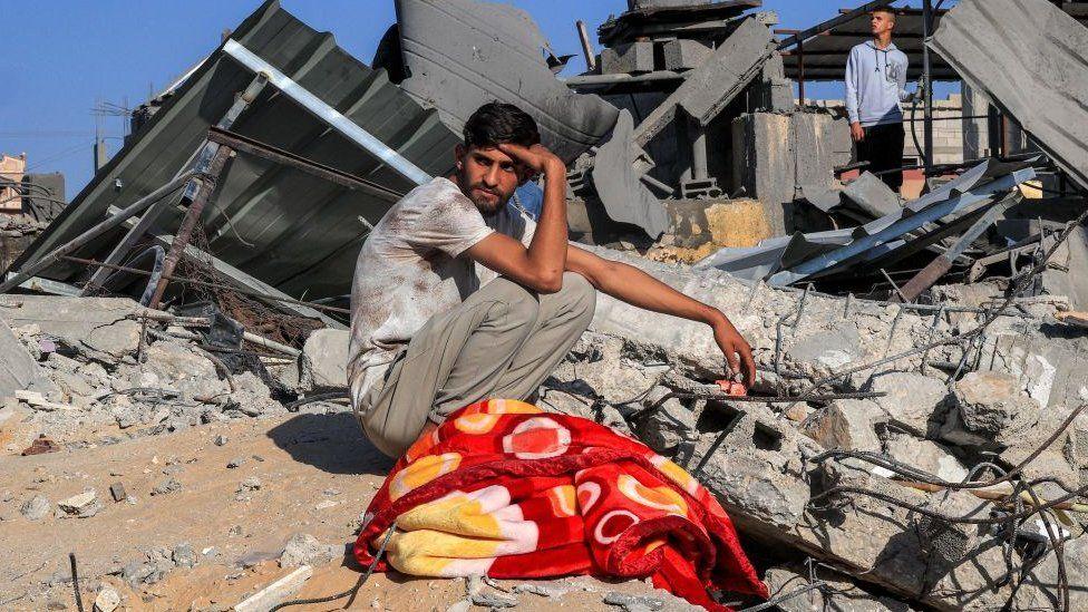 Un joven palestino sentado sobre los escombros de un edificio bombardeado por Israel en el sur de Gaza