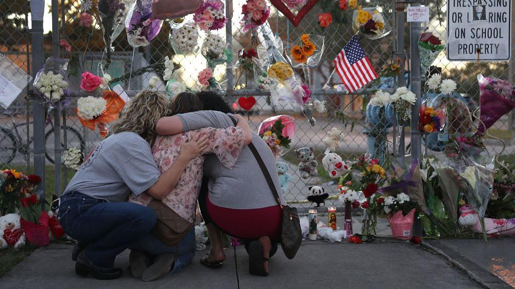 Mujeres se abrazan frente a una pared de recuerdos en honor a víctimas del tiroteo de Marjory Stoneman Douglas 