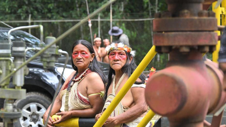 Dos mujeres indígenas miran hacia una conducción de petróleo en el Parque Nacional Yasuní. 