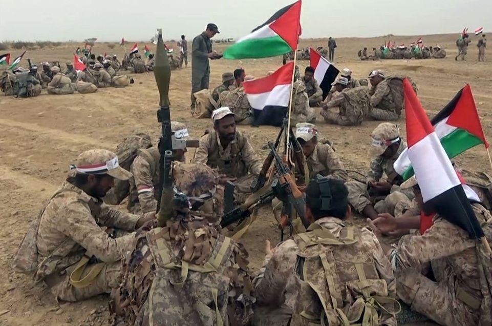 Combatientes hutíes sentados alrededor de una bandera.