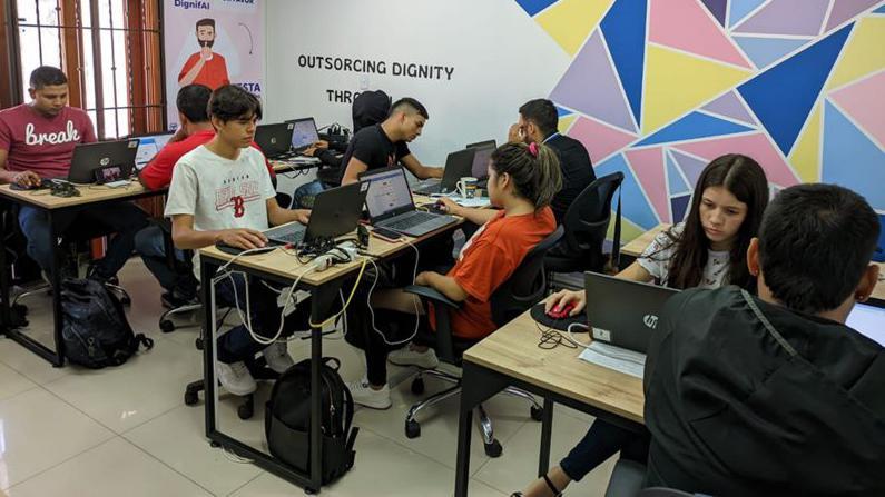 Vários jovens sentados em três mesas com laptops, com feições sérias