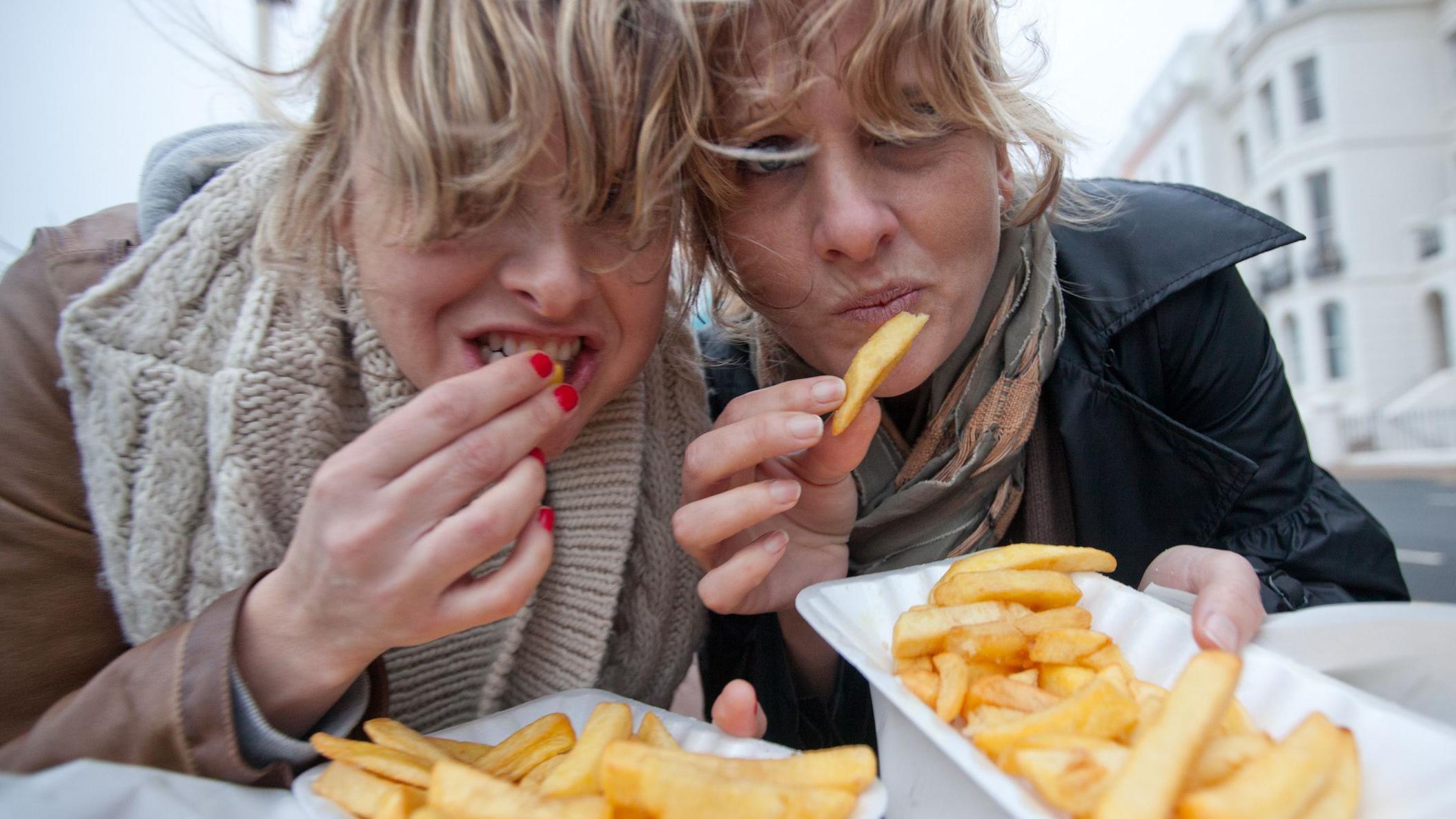 Dos mujeres comen papas fritas. 