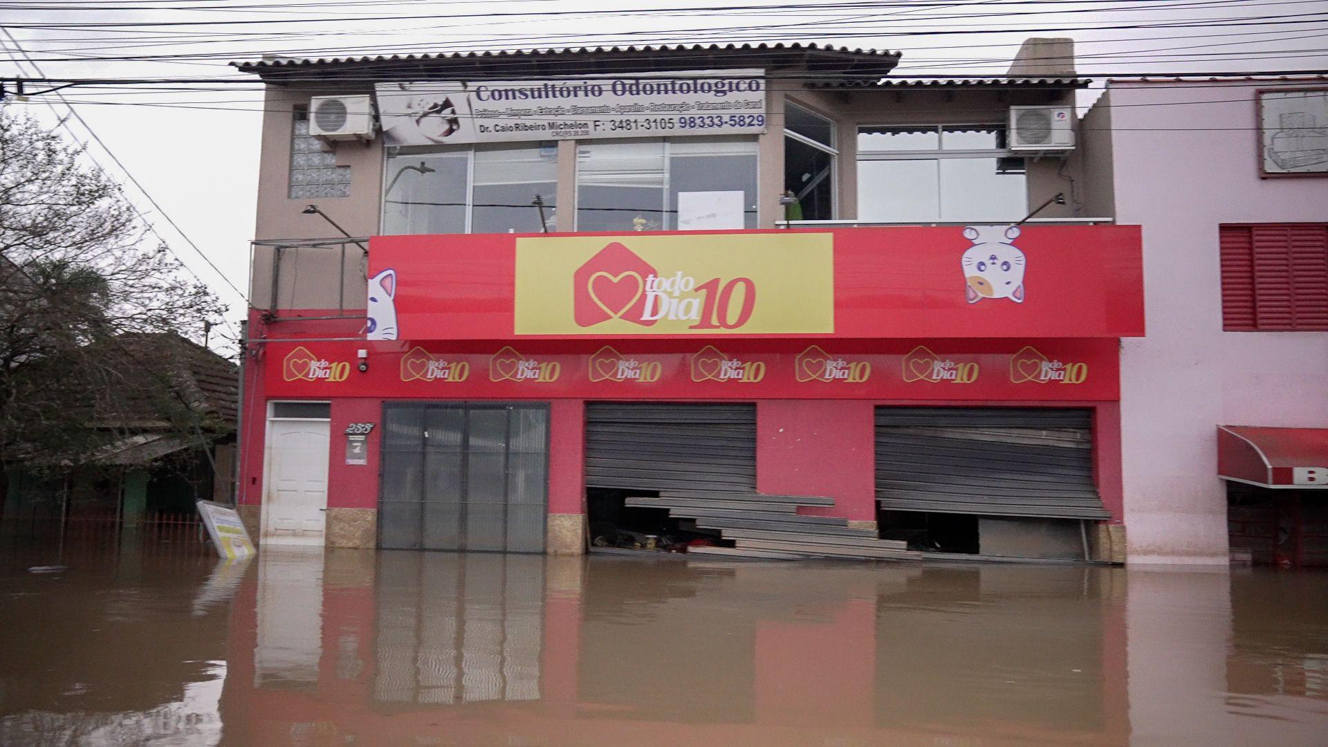 Foto colorida mostra sobrado comercial com a porta estourada em uma rua alagada