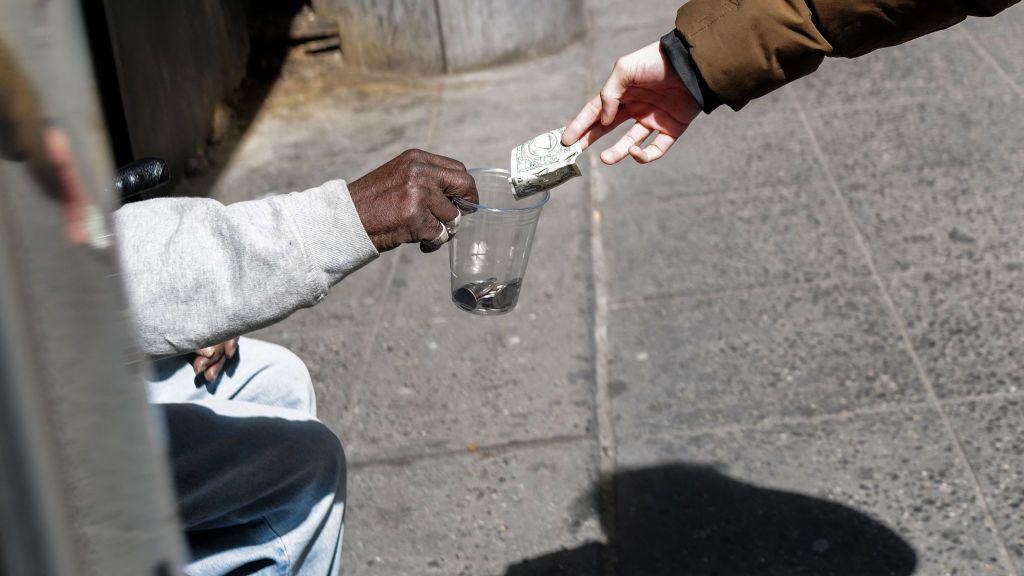 Un hombre da dinero a otro que pide en la calle.