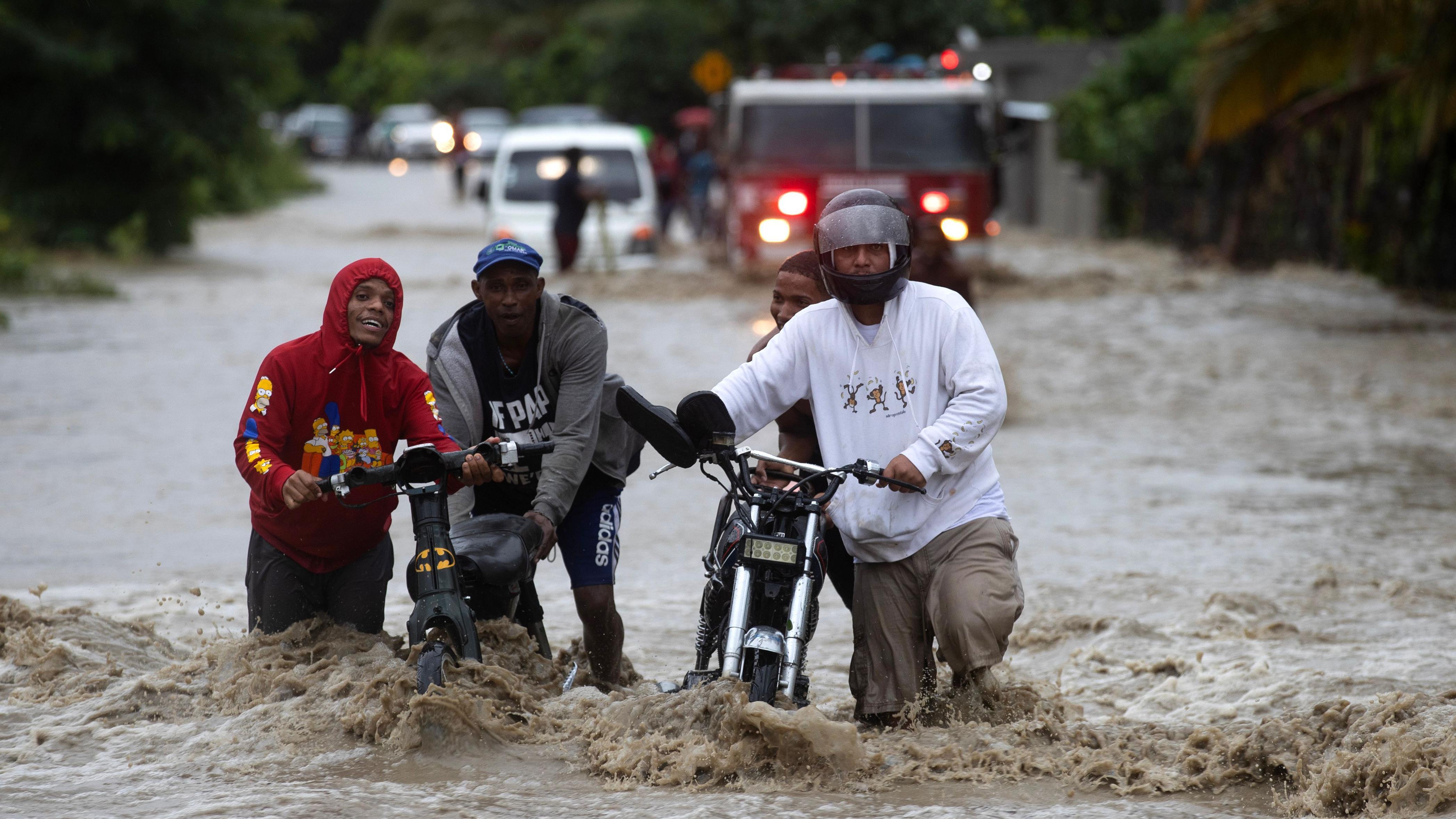 Hombres llevando una motocicleta en una carretera totalmente inundada.