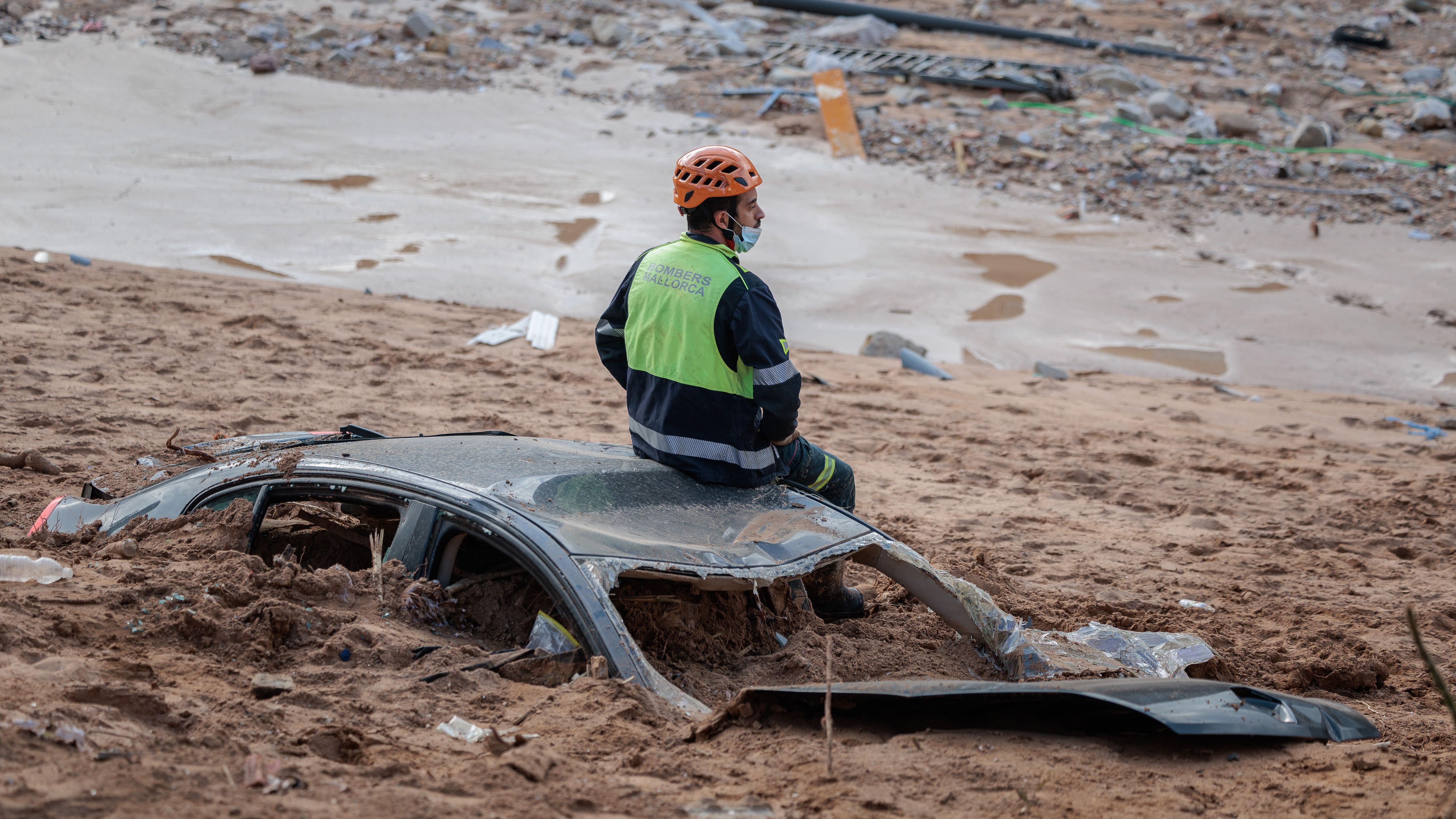 Foto mostra um socorrista sentado em cima de um carro enterrado na lama após inundações repentinas em Valência, Espanha