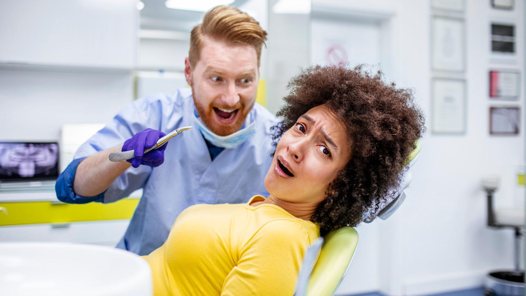 A woman on a dentist's chair looks scared as the dentist approaches her holding a pair of pliers