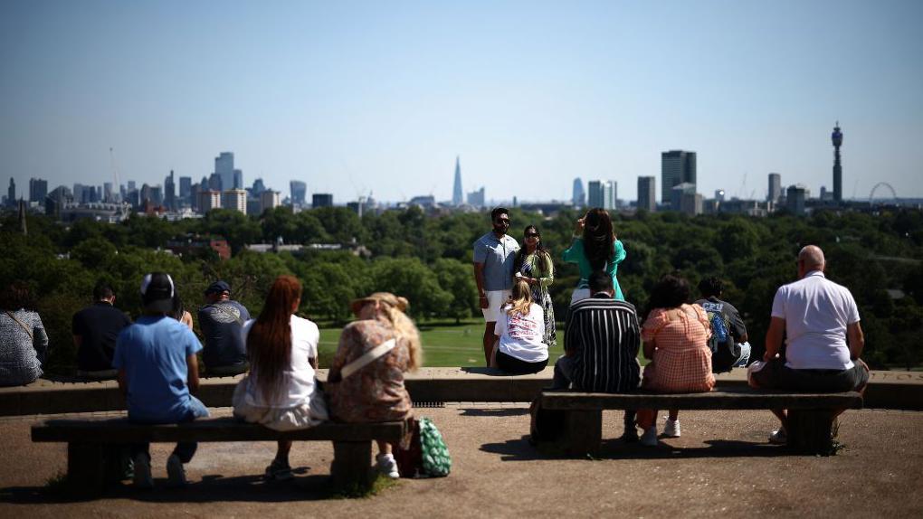 Pessoas sentadas em bancos admirando a vista do horizonte de Londres no Primrose Hill Park