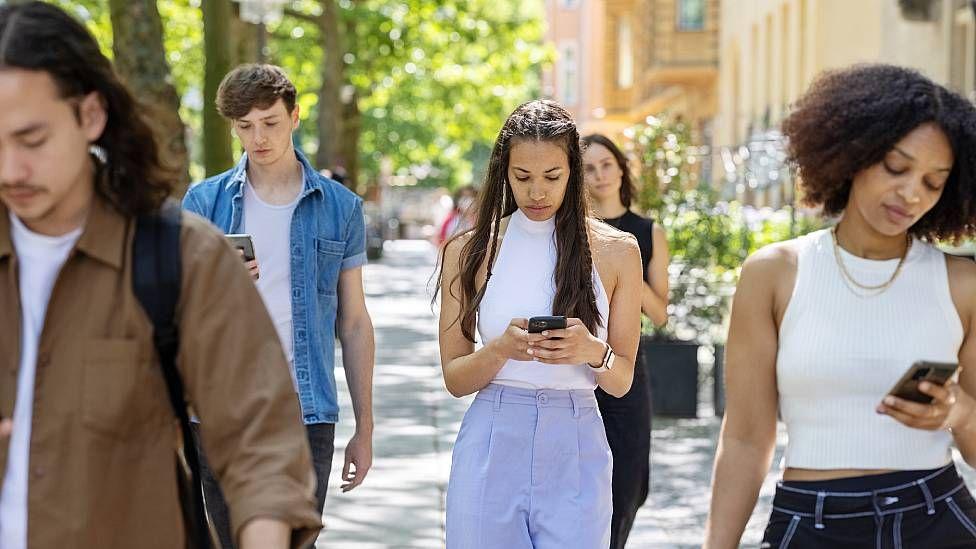 Jóvenes caminando en la calle mirando su celular