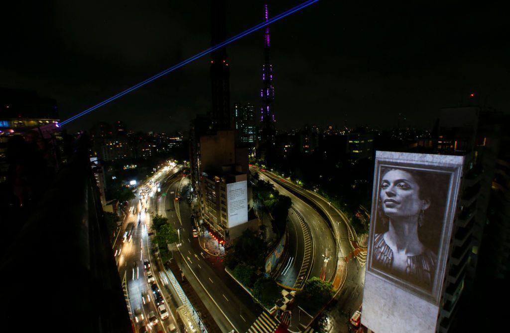 Grafite com rosto de Marielle em prédio, em foto noturna em meio a ruas iluminadas