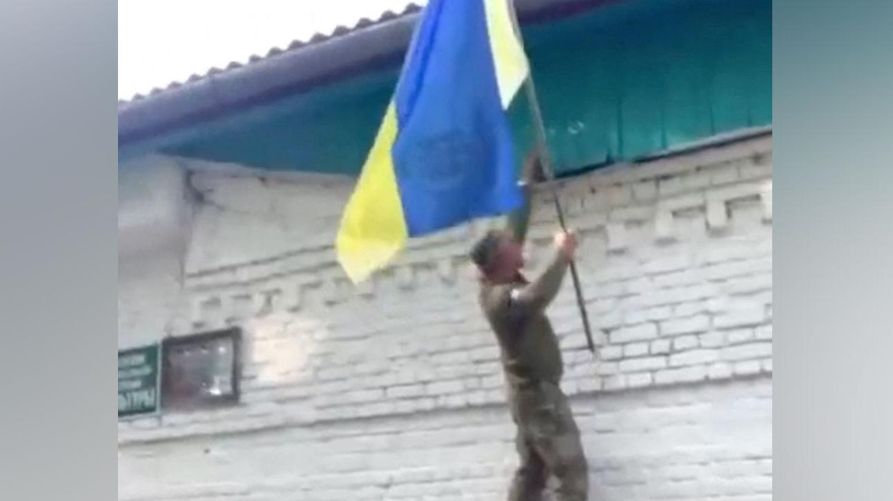 Um soldado ucraniano coloca uma bandeira nacional em um prédio em um vilarejo russo