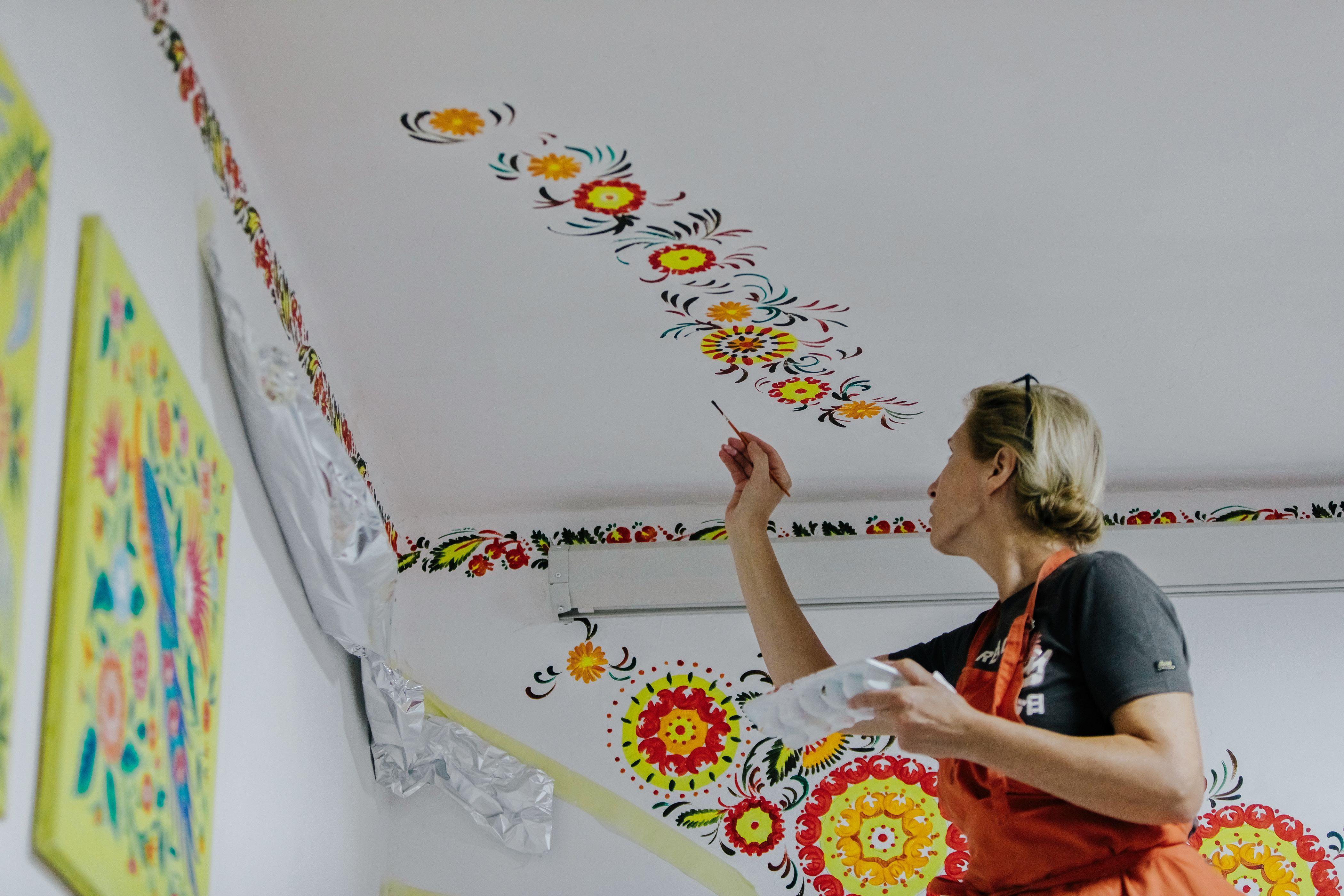 Una mujer hace dibujos en la pared del centro infantil Uniendo Corazones.