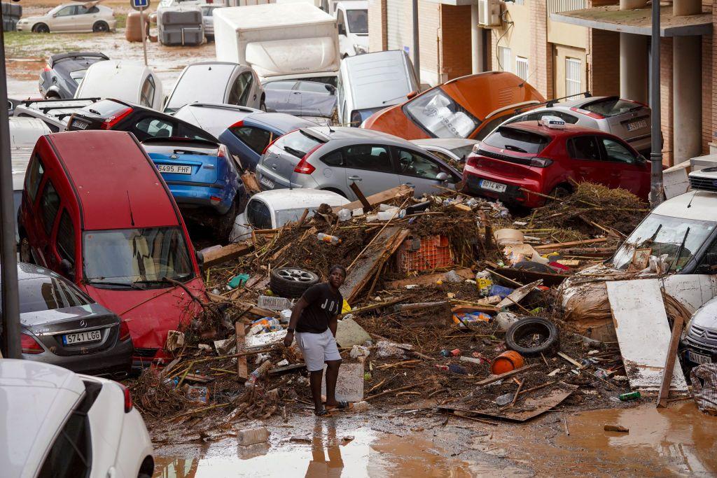 Homem em meio à lama, carros amontoados e entulhos em uma rua