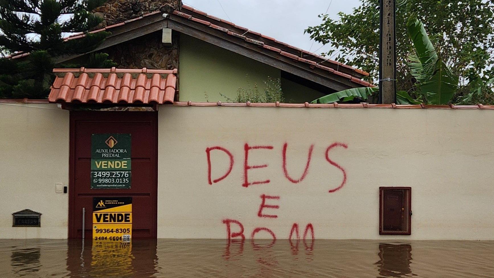 Água cobre parte do muro de casa alagada com os dizeres 