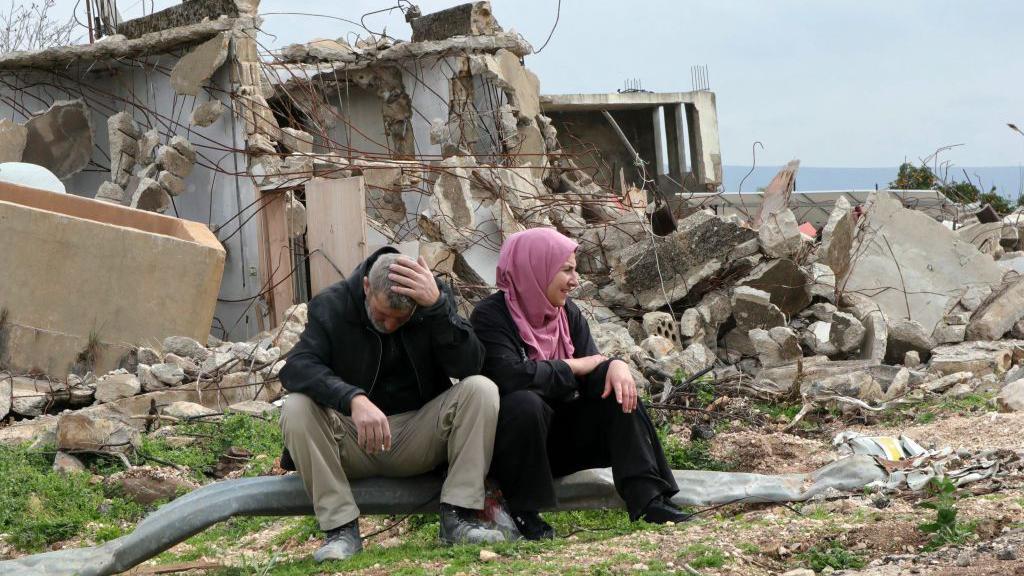 يجلس أفراد عائلة أمام منزلهم المدمر في قرية الوزاني الحدودية بجنوب لبنان بعد انسحاب القوات الإسرائيلية، في 19 فبراير 2025

