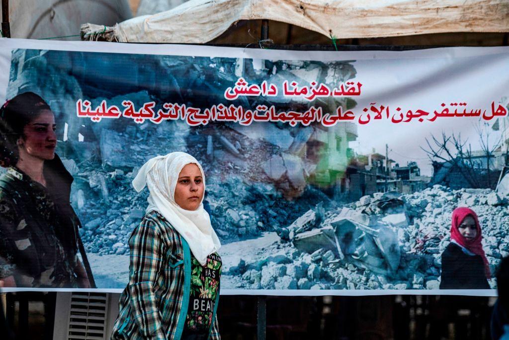 امرأة محجبة تمشي في الشارع أمام لافتة.