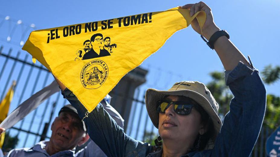 Una mujer se manifiesta con un pañuelo amarillo en el que se lee "El oro no se toma" contra la intención del presidente Nayib Bukele de levantar la prohibición de la minería metálica ante la Asamblea Legislativa, en San Salvador, El Salvador, el 10 de diciembre de 2024. (Foto de Daniela RODRIGUEZ / AFP vía Getty Images).