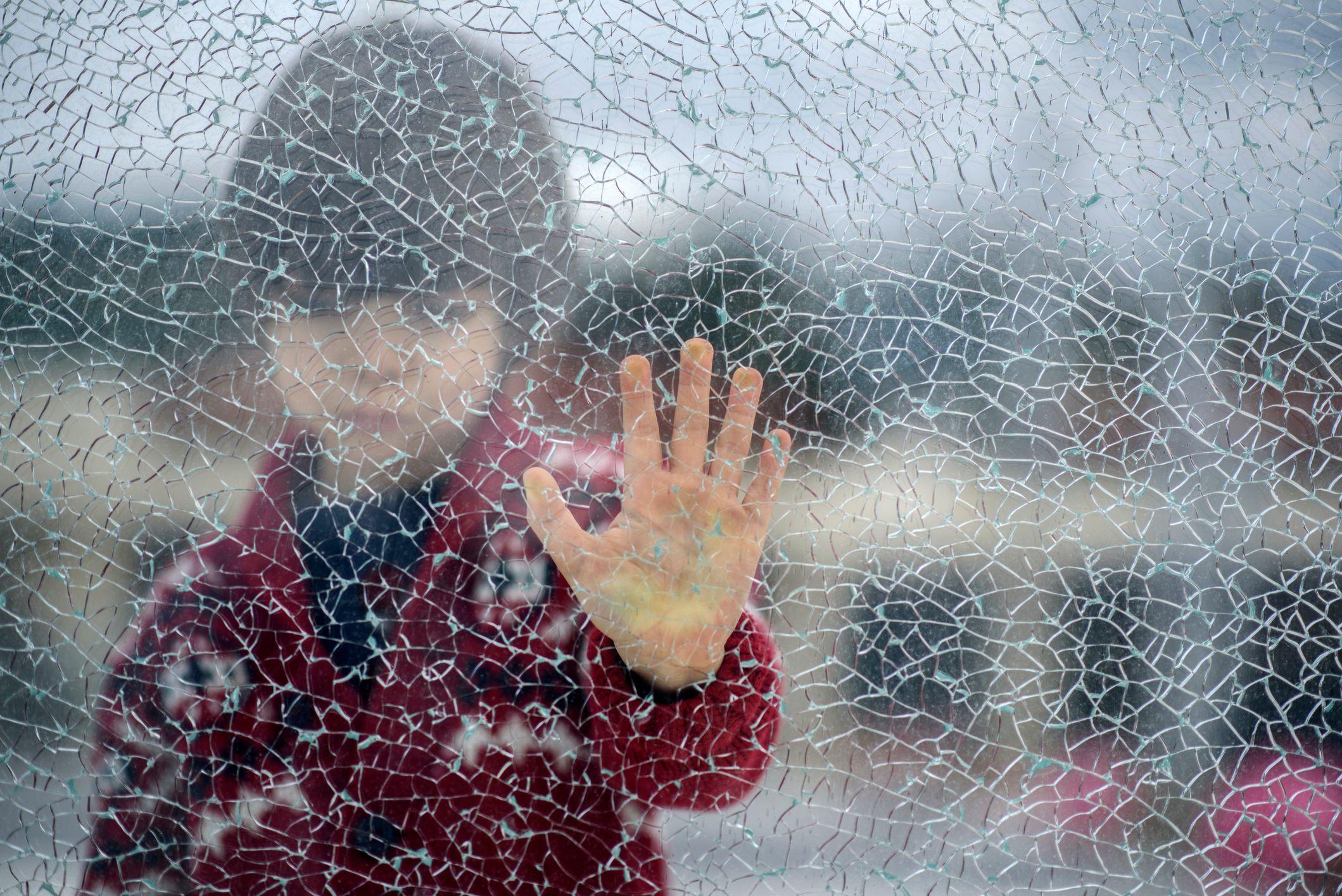 Criança sozinha vista através de vidro quebrado