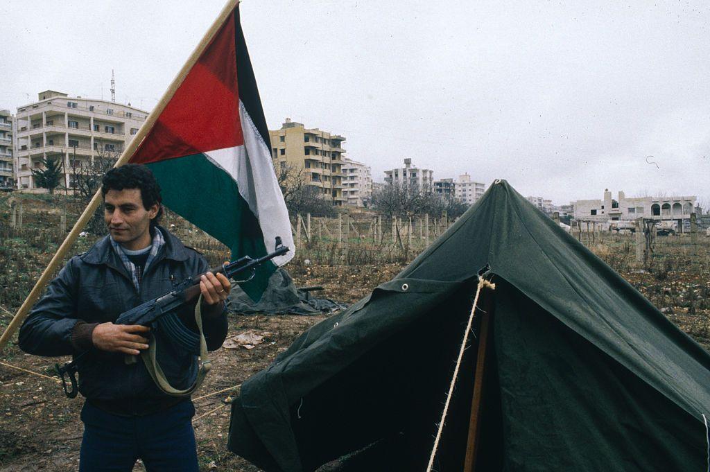 عضو منظمة التحرير الفلسطينية جمال جبارة يحمل رشاشاً، بجوار خيمة وعلم فلسطيني.