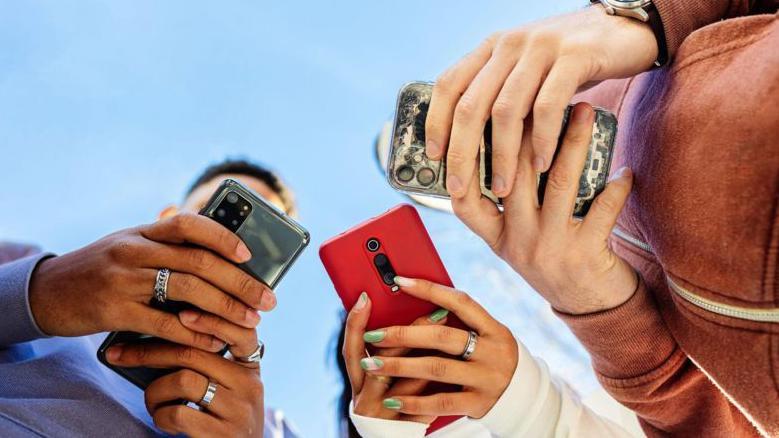 Manos de tres personas que sujetan celulares.
