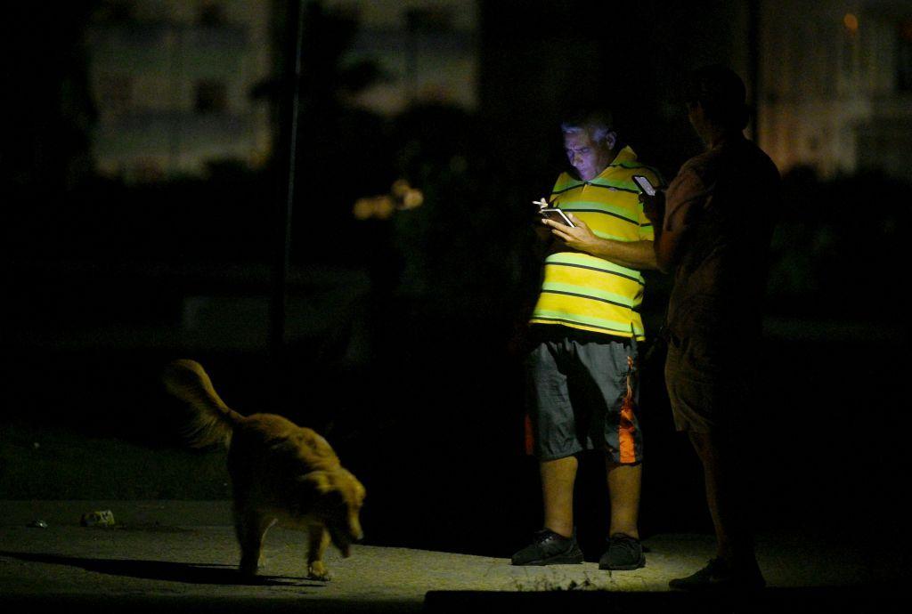 Hombre mirando su teléfono alumbrado con el teléfono de otro hombre en medio del apagón en Cuba.