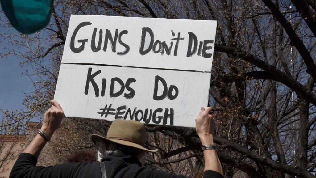 Pancarta en una marcha dice: Las armas no mueren, los niños sí.