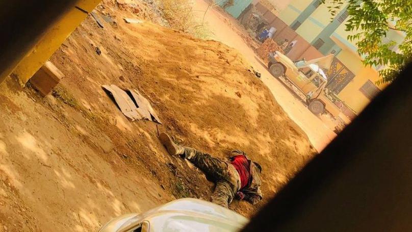 Jenazah prajurit terbaring di tengah jalan, sementara seorang prajurit lain di seberang jalan menggunakan tembok gedung sebagai pelindung di Khartoum pada 15 April, saat kekerasan semakin memuncak