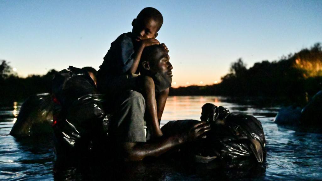 Migrante no rio com os filhos nos braços