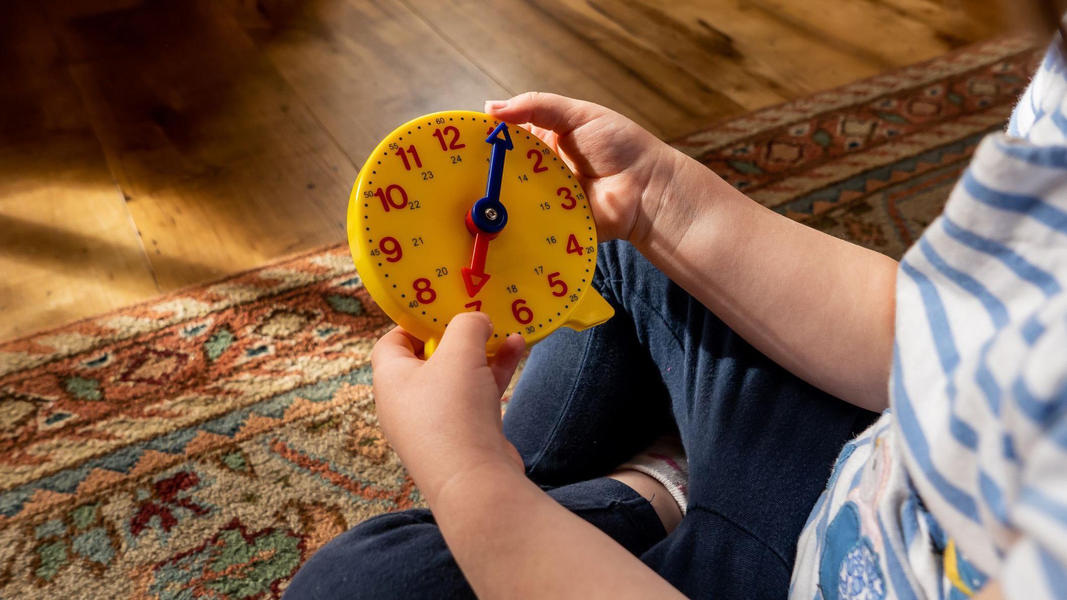 Mão de criança segurando relógio de brinquedo.