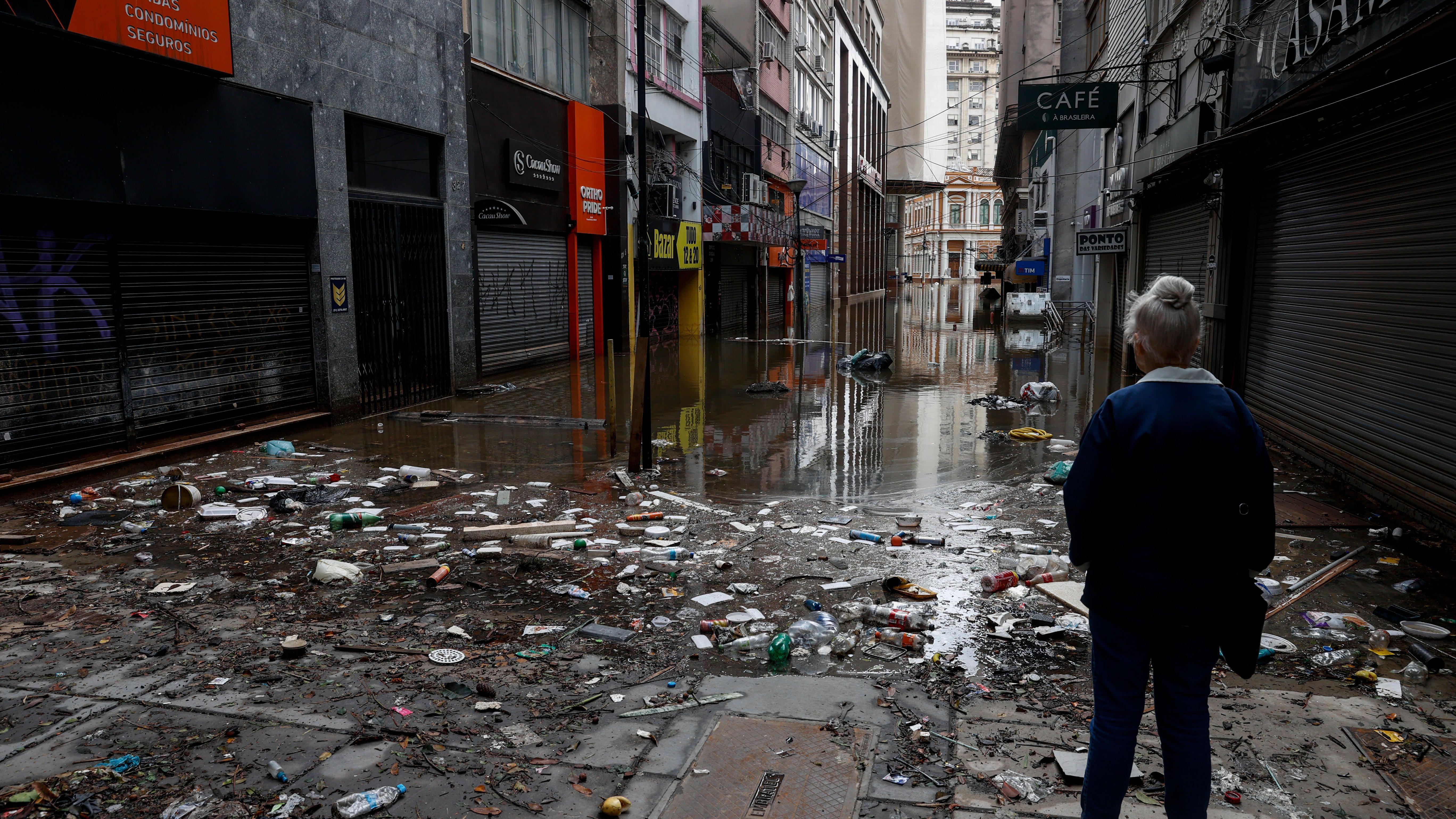 Pessoa observa rua destruída e água de inundação abaixando